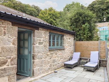 A stone exterior with a blue door and window next to two cushioned lounge chairs and a small table on a patio at Pendeen in Mawnan Smith Near Falmouth
