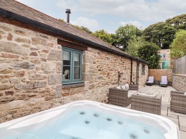 A stone wall patio with a hot tub rattan seating and two lounge chairs at Pendeen in Mawnan Smith Near Falmouth