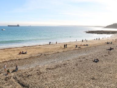 A sandy beach with people sitting and walking near the ocean with ships in the distance at Pendeen in Mawnan Smith Near Falmouth