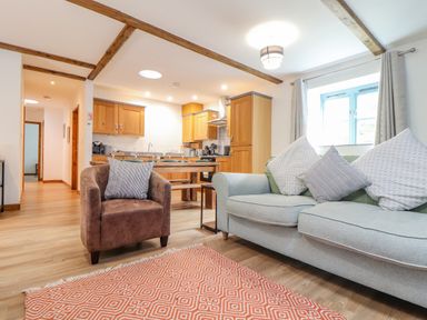 An open living room and kitchen with a gray sofa and a brown armchair at Budock in Mawnan Smith Near Falmouth