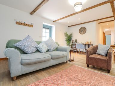 A living room with a grey sofa and brown armchair with cushions a desk and chairs in the background at Budock in Mawnan Smith Near Falmouth