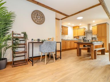 An open kitchen and dining area with wooden cabinets a wooden dining table and a desk with a chair and plants at Budock in Mawnan Smith Near Falmouth