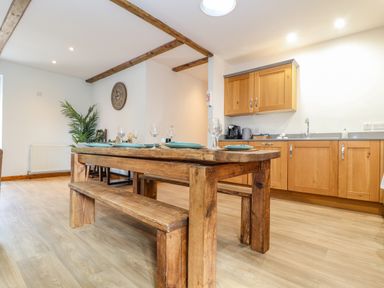 A kitchen with wooden cabinets a wooden dining table and bench with glassware and plates at Budock in Mawnan Smith Near Falmouth