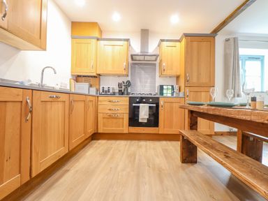 A kitchen with wooden cabinets a gas stove a wooden dining table and bench at Budock in Mawnan Smith Near Falmouth
