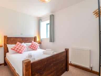 A bedroom with a wooden bed frame white bedding red checkered pillows and rolled white towels at Budock in Mawnan Smith Near Falmouth