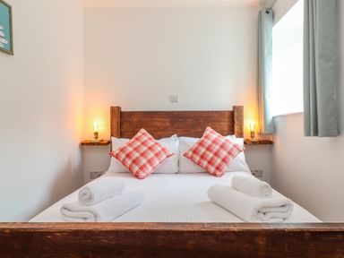 A bedroom with a double bed with wooden headboard and red checkered cushions at Budock in Mawnan Smith Near Falmouth