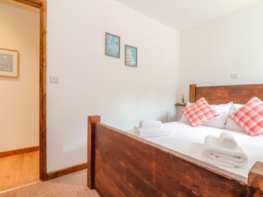 A bedroom with a wooden bed frame with white bedding and red checkered pillows with folded white towels on the bed and framed pictures on the wall at Budock in Mawnan Smith Near Falmouth