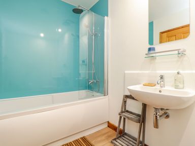 A bathroom with a bathtub shower combination and a sink with a mirror shelf and wooden floor at Budock in Mawnan Smith Near Falmouth