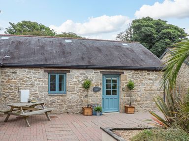 Stone cottage with blue door and window on a brick patio with picnic table and potted plants at Budock in Mawnan Smith Near Falmouth
