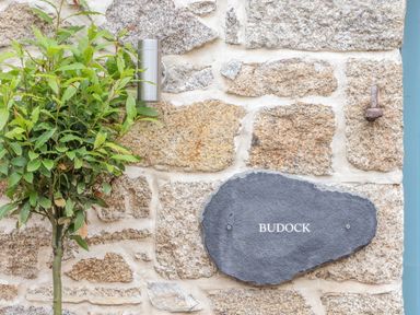 A stone wall with a small tree a metal light fixture and a stone plaque reading Budock at Budock in Mawnan Smith Near Falmouth