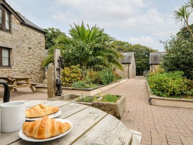 A stone courtyard with plants and palm trees and croissants on a wooden table at Kerensa in Mawnan Smith Near Falmouth