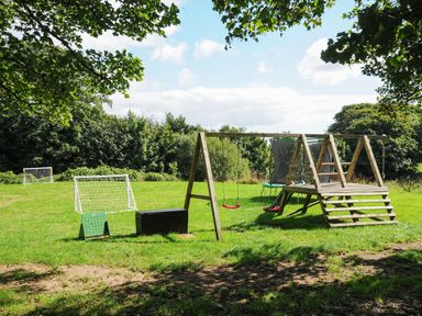 A grassy outdoor area with a wooden swing set slides and soccer goals at Kerensa in Mawnan Smith Near Falmouth