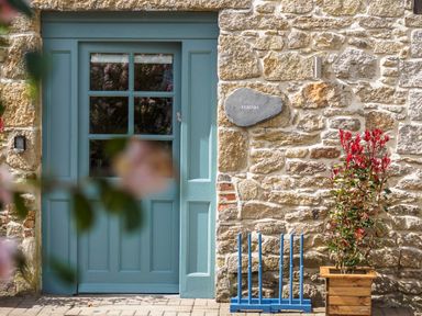 A blue door set in a stone wall with a plant in a wooden pot and a blue croquet set at Kerensa in Mawnan Smith Near Falmouth