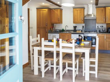 A kitchen with wooden cabinets a dining table set with food and drinks at Kerensa in Mawnan Smith near Falmouth