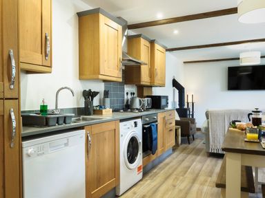 A kitchen and living area with wooden cabinets appliances a dining table and a television at Kerensa in Mawnan Smith Near Falmouth