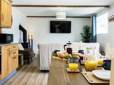 A kitchen and dining area with a breakfast table set with croissants orange juice and coffee at Kerensa in Mawnan Smith Near Falmouth