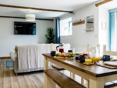 A dining table set with breakfast items and a living room with a sofa and wall-mounted TV at Kerensa in Mawnan Smith Near Falmouth