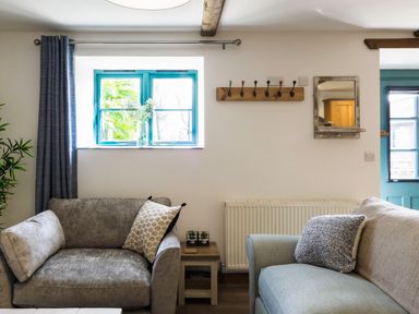 A living room with two sofas a side table a window with curtains and a wall mirror at Kerensa in Mawnan Smith Near Falmouth