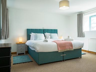 A bedroom with a teal bed two nightstands with lamps and two windows at Kerensa in Mawnan Smith Near Falmouth