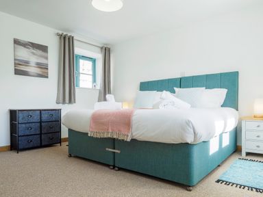 A bedroom with a large bed with white bedding and a teal upholstered base at Kerensa in Mawnan Smith Near Falmouth