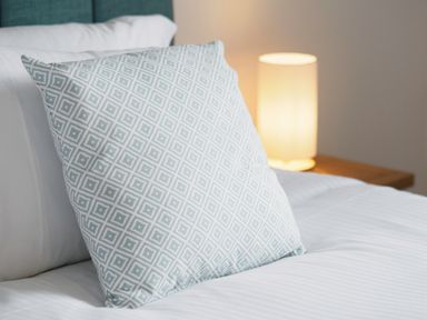 A bed with a patterned pillow and a lit bedside lamp at Kerensa in Mawnan Smith Near Falmouth