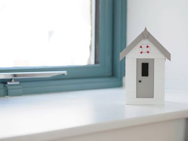 A small decorative white and gray house with a door and life preserver on a white surface near a window
