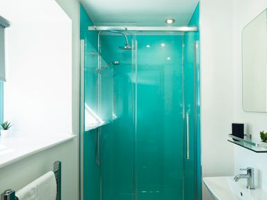 A bathroom with a glass door shower with blue walls a white sink a mirror and a towel rack at Kerensa in Mawnan Smith Near Falmouth