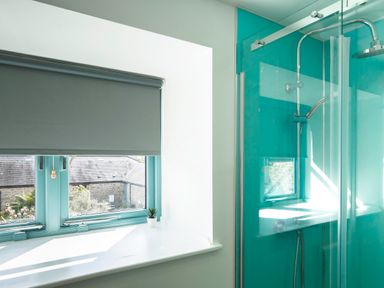 A bathroom window with a small plant and a shower area with turquoise walls at Kerensa in Mawnan Smith Near Falmouth
