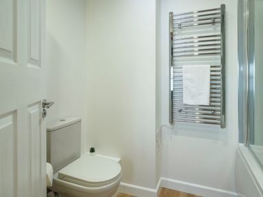 A bathroom with a toilet a small plant on the toilet tank a heated towel rail with a white towel and a bathtub at Kerensa in Mawnan Smith Near Falmouth