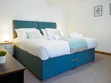 A bedroom with a double bed with white bedding and blue headboard and a small plant on a wooden table at Kerensa in Mawnan Smith Near Falmouth