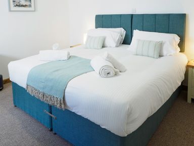 A bedroom with a double bed with blue headboard white bedding rolled towels and a blue throw at Kerensa in Mawnan Smith Near Falmouth