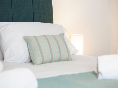 A bed with white pillows and a striped cushion with a lamp in the background at Kerensa in Mawnan Smith Near Falmouth