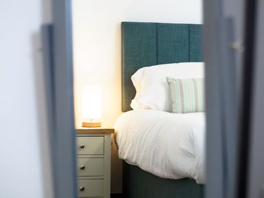 A bed with a green headboard a white pillow with a striped cushion and a lamp on a bedside table at Kerensa in Mawnan Smith Near Falmouth