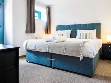 A bedroom with a blue bed and white bedding with rolled towels on top at Kerensa in Mawnan Smith Near Falmouth