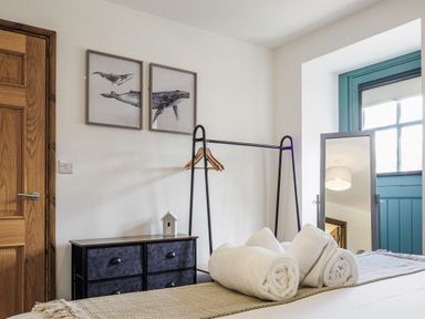 A bedroom with rolled towels on a bed a clothes rack with hangers a dresser and a mirror at Kerensa in Mawnan Smith Near Falmouth
