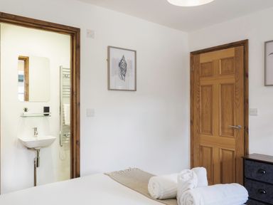 A bedroom with a wooden door a small sink an adjoining bathroom and rolled towels on the bed at Kerensa in Mawnan Smith Near Falmouth