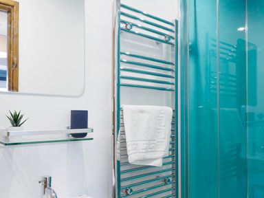 A bathroom with a white towel on a chrome towel rack near a glass shelf with a small plant and a dark container at Kerensa in Mawnan Smith Near Falmouth