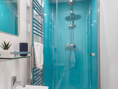 A bathroom shower with blue walls a glass door a towel rack and a sink with a faucet at Kerensa in Mawnan Smith Near Falmouth