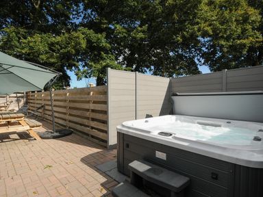 An outdoor patio with a hot tub wooden picnic table umbrella and lounge chairs at Newlyn in Mawnan Smith Near Falmouth