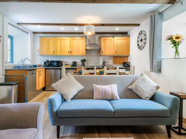 An open plan kitchen and living area with a blue two-seater sofa and wooden cabinets at Newlyn in Mawnan Smith Near Falmouth