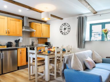 A kitchen dining area with wooden cabinets a dining table with chairs and a blue sofa by a window at Newlyn in Mawnan Smith Near Falmouth