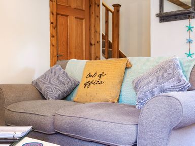 A grey sofa with three cushions and a blanket in a room with a wooden door and staircase at Newlyn in Mawnan Smith Near Falmouth