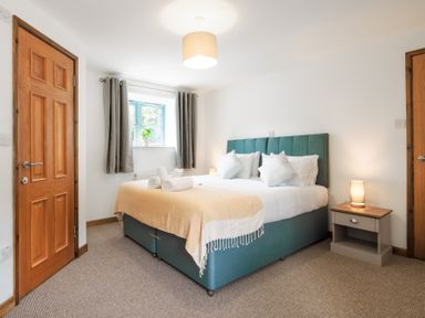 A bedroom with a bed with pillows and towels a nightstand with a lamp and a window with curtains at Newlyn Mawnan Smith Near Falmouth