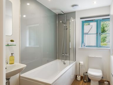 A bathroom with a bathtub shower sink and toilet near a window with blue frames at Newlyn in Mawnan Smith Near Falmouth