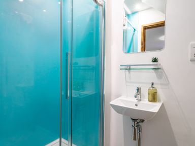A bathroom with a blue shower enclosure a white sink with soap dispenser and a mirror above at Newlyn in Mawnan Smith Near Falmouth