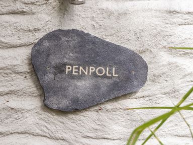 A dark stone plaque with the word Penpoll mounted on a textured white wall with some green leaves in the corner at Penpoll in Falmouth
