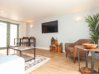 A living room with a wall-mounted TV a brown armchair wooden side tables and a table with two chairs at Penpoll in Falmouth