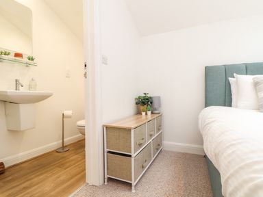 A bedroom corner with a storage unit next to a bed and a bathroom with a sink and toilet visible through an open door at Penpoll in Falmouth