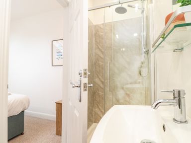 A bathroom with a sink and shower visible through an open door leading to a bedroom with a bed and a wooden nightstand at Penpoll in Falmouth