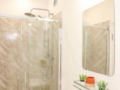 A bathroom with a glass enclosed shower and a mirror above a shelf with potted plants at Penpoll in Falmouth